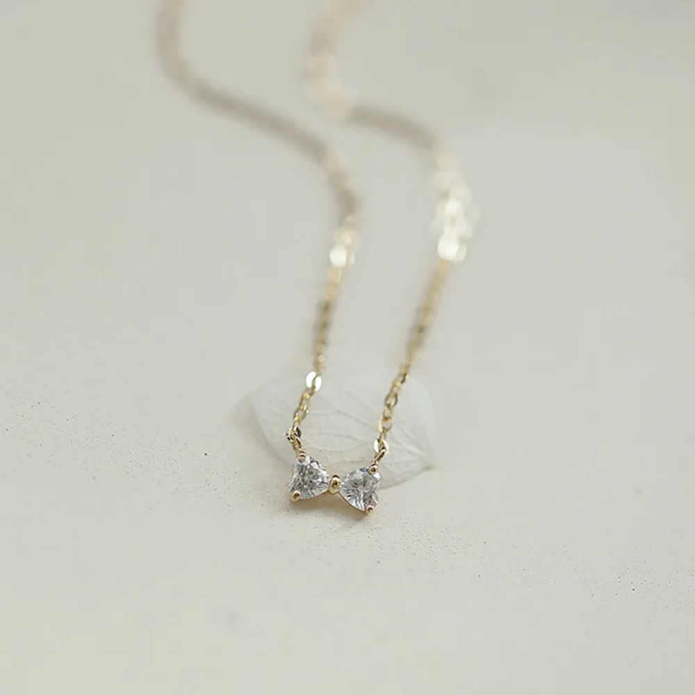 Gold necklace with heart-shaped pendants on a light gray background