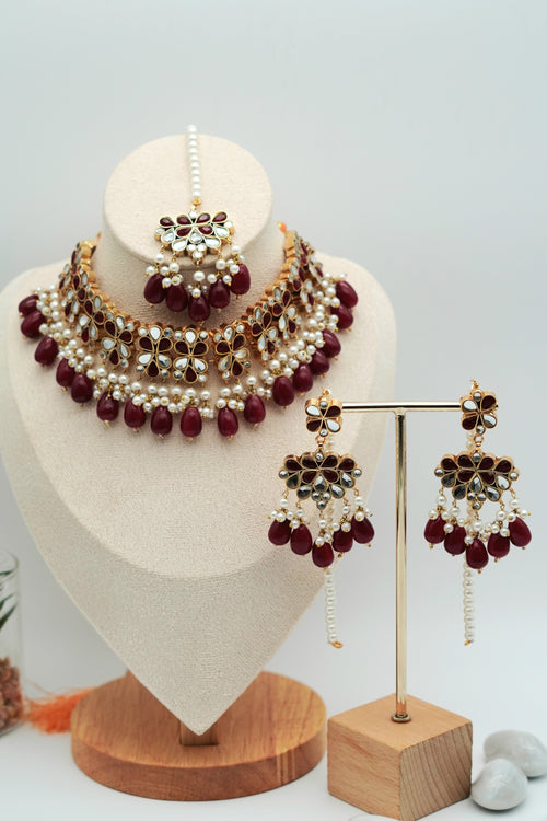 Jewelry set with maroon and gold elements on a mannequin bust and stand.