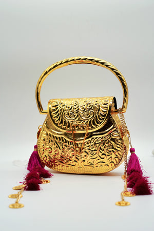 Gold handbag with intricate designs and pink tassels on a light gray background